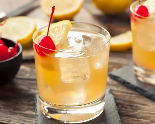 En gyllene whiskey sour med is, citron och körsbär. En klassisk drink som passar perfekt en varm dag.