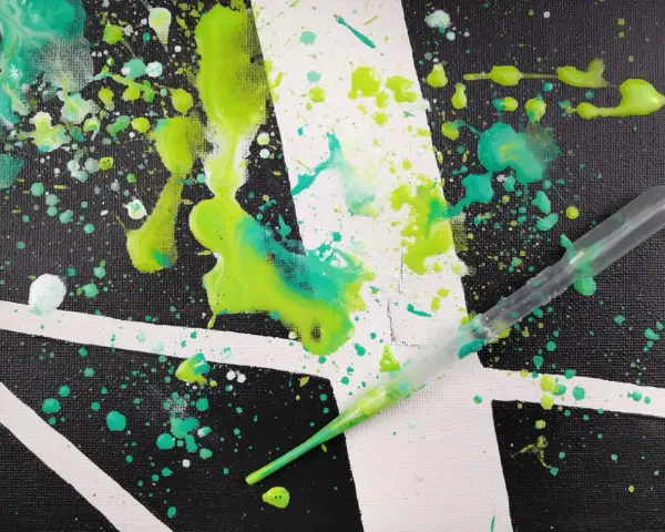 Projection de peinture sur toile, avec des éclaboussures vertes et turquoise sur un fond noir et blanc. Une pipette est visible, prête à projeter plus de peinture.