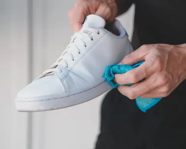 Mani che puliscono una scarpa bianca Adidas Stan Smith con un panno blu. Ecco come lavare le Stan Smith per farle tornare come nuove.