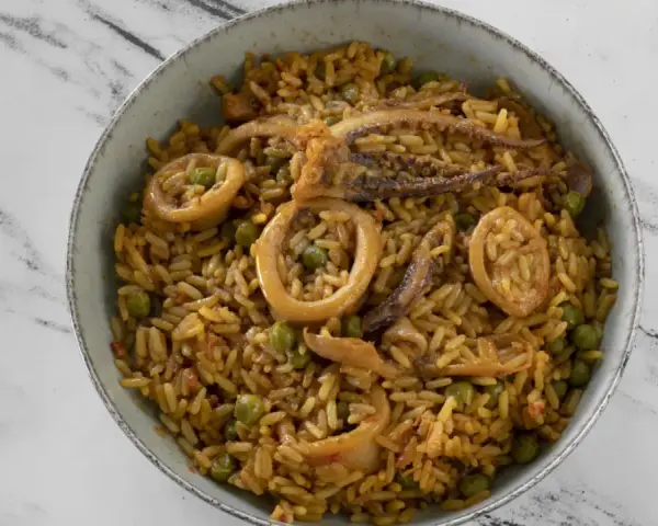 Un delicioso plato de arroz con calamares y guisantes, servido en un cuenco sobre una superficie de mármol.