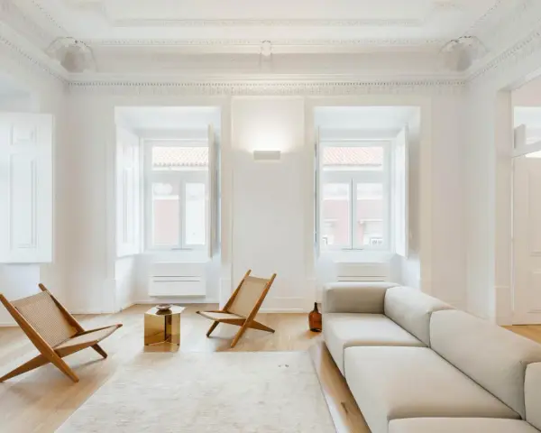 Ecco cosa fa l'architetto d'interni: crea un soggiorno minimalista con divano chiaro, sedie in legno e un tavolino dorato, valorizzando la luce naturale.
