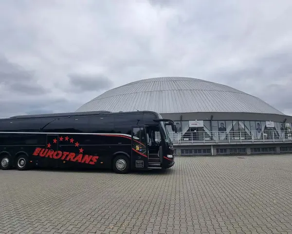 Czarny autokar firmy Eurotrans przed nowoczesnym budynkiem z kopułą.
