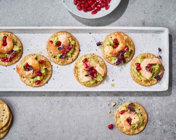 Mediterranes Fingerfood kalt: Garnelen auf Avocado-Creme mit Granatapfelkernen und Kräutern auf Crackern.