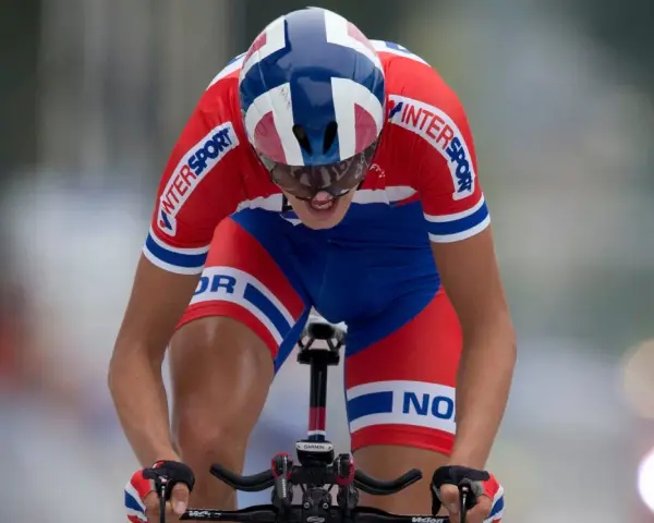 Oskar Svendsen, a cyclist in a red and blue Norwegian kit, races intensely, focused on the finish line.