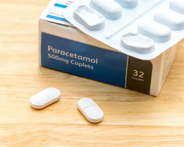 Opakowanie paracetamolu 500mg i dwie tabletki na drewnianym tle. Szybka ulga w bólu zęba.