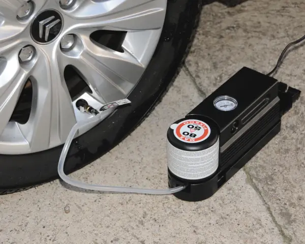 Riparazione di una gomma bucata con kit di gonfiaggio. Il compressore è collegato alla valvola del pneumatico.