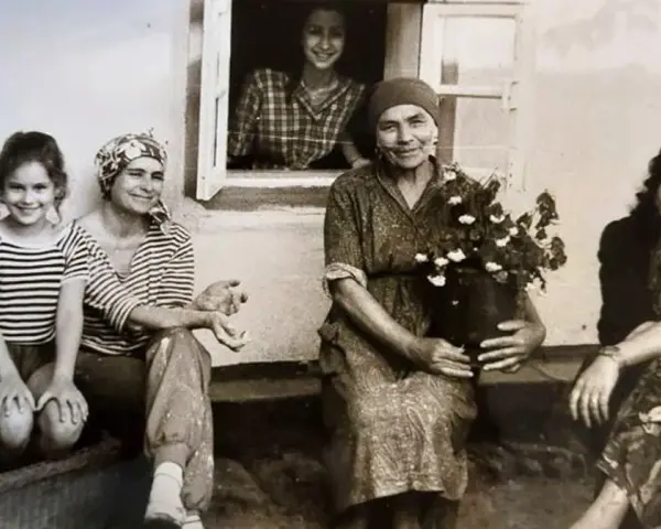 Maria Wojewodzka z rodziną na tle domu. Kobiety w różnym wieku, jedna z nich trzyma kwiaty.
