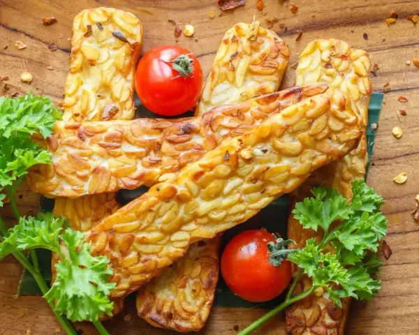 Złocisty, smażony tempeh, czyli co to jest? Podany z pomidorkami i natką pietruszki na drewnianej desce.