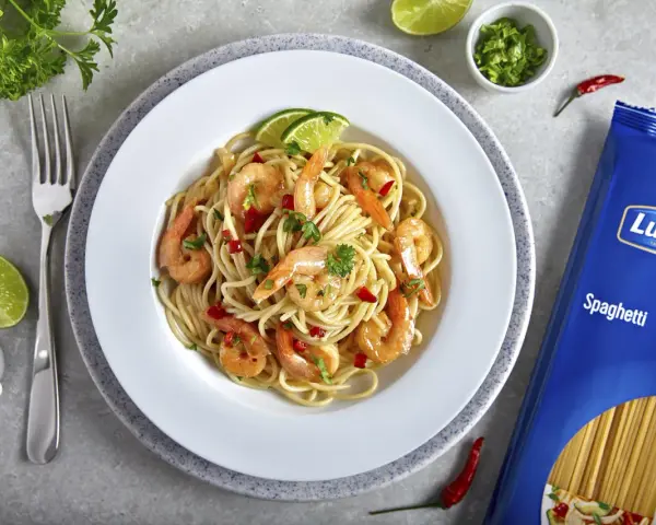 Pyszny makaron z krewetkami na winie, udekorowany limonką i natką pietruszki. Obok opakowanie makaronu spaghetti Lubella.