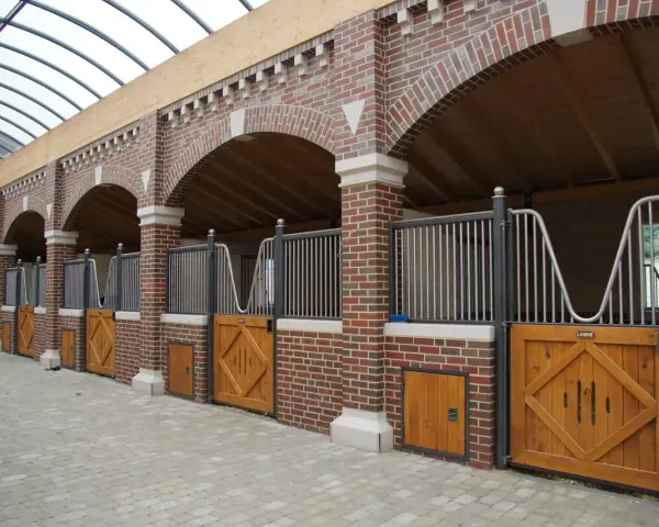 Belle écurie pour chevaux avec des boxes en briques rouges, des portes en bois et un toit transparent.