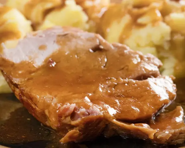 Mięciutka karkówka w sosie, podana z purée ziemniaczanym. Danie wygląda apetycznie i soczyście.