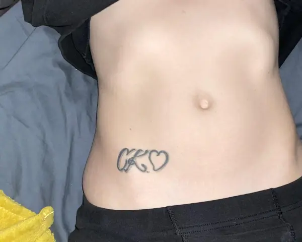 Tatuaz inicjaly CK wplecione w serduszka na brzuchu.
