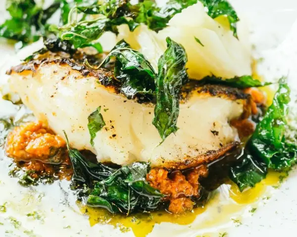 Delicioso bacalao al pil pil, con su piel dorada, acompañado de verduras frescas y una salsa vibrante.