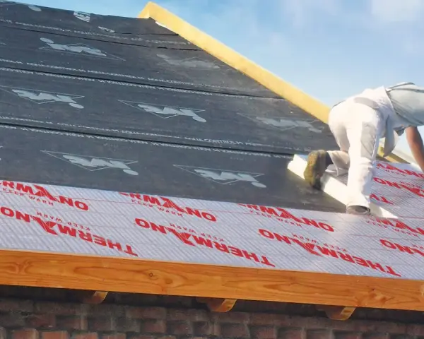 Pracownik montuje ocieplenie nakrokwiowe na dachu, układając warstwy izolacji i membrany.