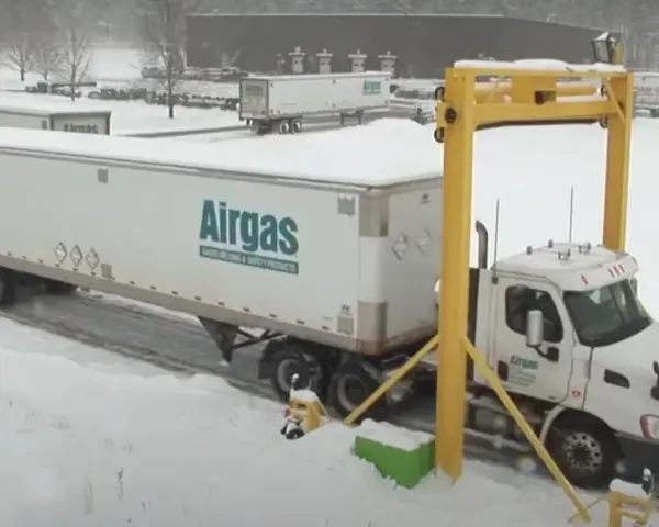 Ciężarówka z naczepą Airgas pod żółtą bramownicą w śnieżny dzień.