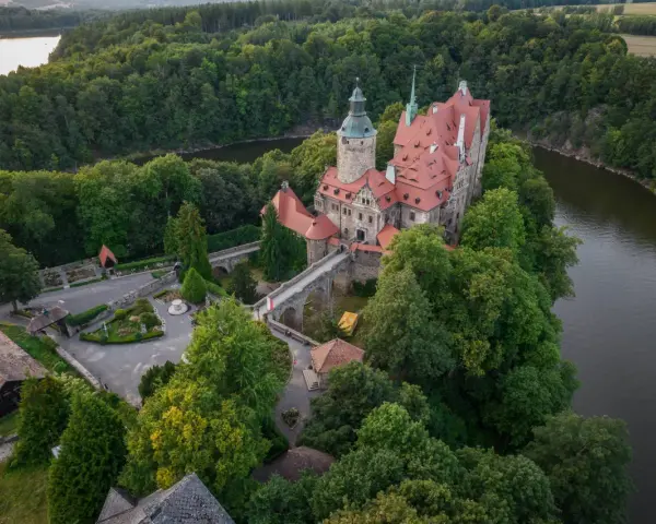 Zamek Czocha, malowniczo położony na skalistym cyplu nad rzeką, otoczony bujną zielenią.