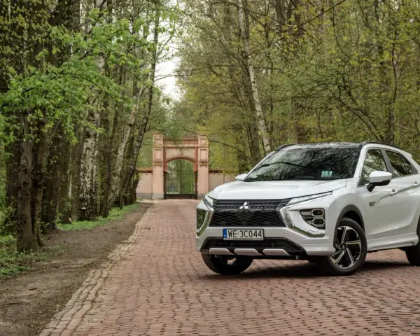 Biały Mitsubishi Eclipse Cross na tle bramy i drzew. Wiele pozytywnych mitsubishi eclipse cross opinie potwierdza jego wszechstronność.