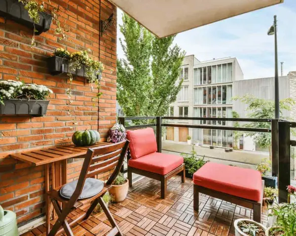 Arredare terrazzo appartamento: un angolo relax con sedie rosse, tavolino in legno e piante su muro di mattoni.