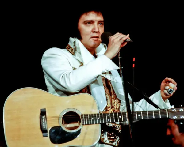 Elvis Presley singt mit Gitarre und Mikrofon, ein Bild, das sein immenses Vermögen symbolisiert.