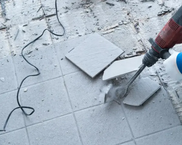 Skuwanie płytek młotem udarowym. Widać fragmenty rozbijanej podłogi i kabel zasilający.