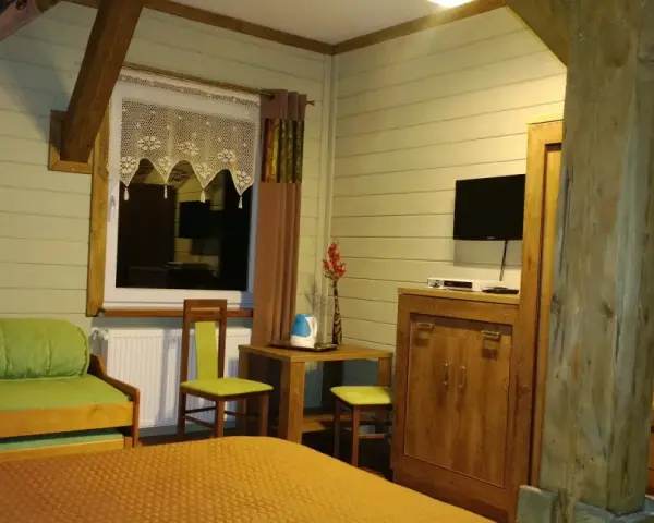 Przytulny pokój w schronisku Śnieżne Kotły. Zielona kanapa, drewniane meble i widok z okna.