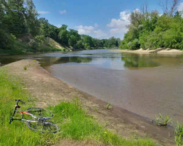 Rower leży na trawie nad rzeką, otoczoną zielenią. To malowniczy zakątek, prawdziwa szwajcaria podlaska.