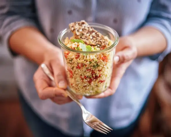 Un bocal rempli de quinoa coloré, parfait pour un régime sain. Une fourchette est prête à déguster ce plat savoureux.
