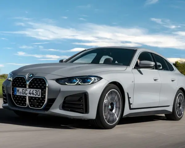 Eleganckie, szare BMW Gran Coupé sunie po drodze na tle błękitnego nieba z chmurami.