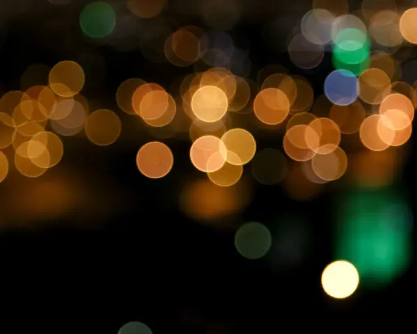 Des lumières de ville floues créent un arrière-plan bokeh chaleureux, avec des cercles dorés, verts et bleus sur fond noir.