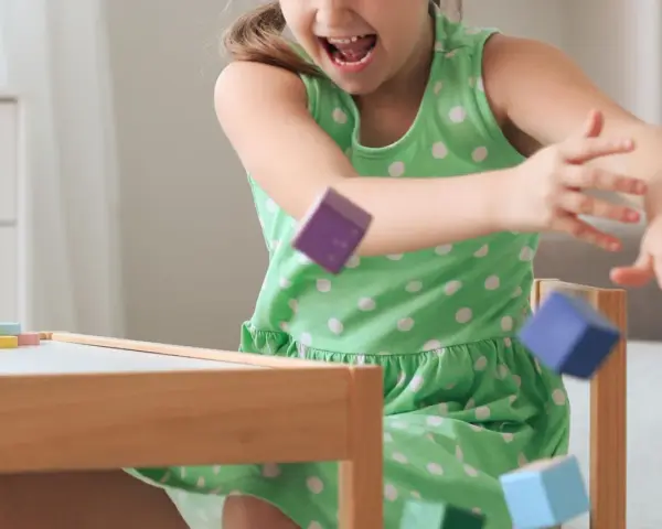 Ein Mädchen in einem grünen Kleid wirft bunte Holzklötze. Ein Versuch, laute Kinder zur Ruhe zu bringen, indem man sie zum Spielen anregt.