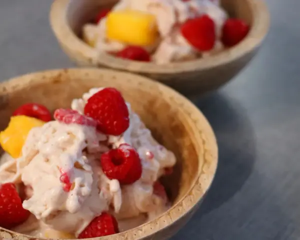 Två skålar med krämig proteinglass, toppad med hallon och mangobitar. Ett perfekt recept för en hälsosam dessert.