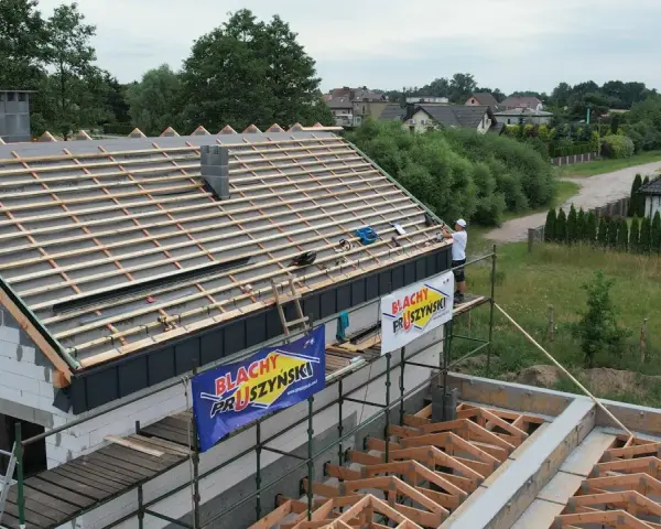 Budowa dachu z blachą i membraną. Pracownik na rusztowaniu montuje pokrycie.