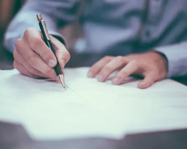 Mano firmando un contrato de reserva de vivienda. El documento se extiende sobre una mesa, con un bolígrafo en acción.
