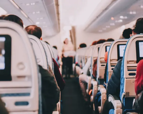 View from inside an airplane cabin, showing rows of seats with passengers and entertainment screens.
