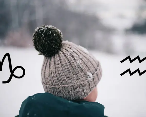 Znak zodiaku Koziorożec i Wodnik, przypominające o tym, jaki znak zodiaku ma styczeń. Dziecko w zimowej czapce na tle śniegu.
