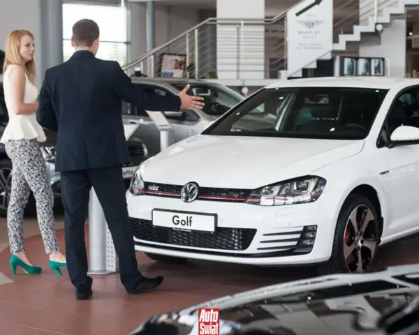 Sprzedawca prezentuje biały samochód flotowy Volkswagen Golf klientce w salonie samochodowym.