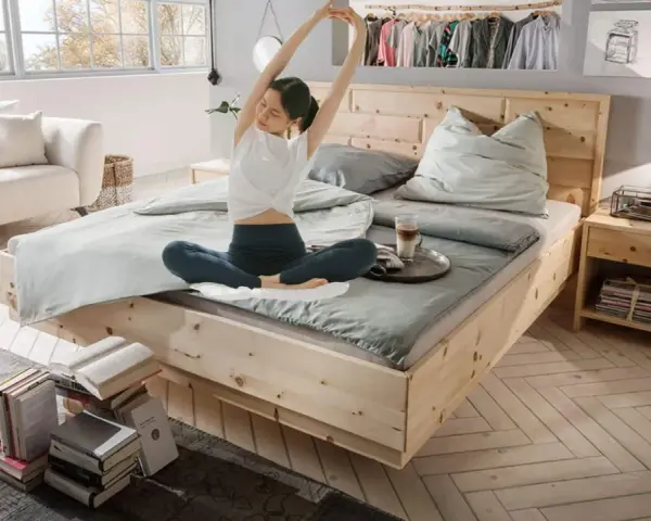 Frau dehnt sich im hellen Schlafzimmer. Ein gemütliches Bett, ein Sofa und Bücher laden zum Entspannen ein. Perfekt, um das Schlafzimmer einzurichten.