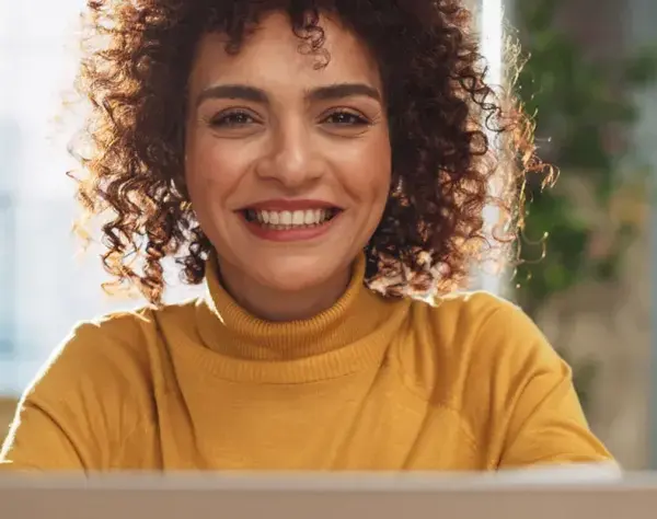 Lächelnde Frau mit Locken am Laptop, bereit für ihre Bewerbung als studentische Hilfskraft.