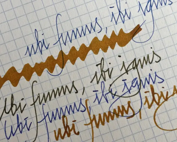 Papel cuadriculado con escritura a mano en tinta azul y marrón. Se lee "ubi fumus, ibi ignis" repetidamente.