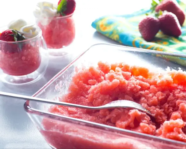 Erfrischende Erdbeer Granita in einer Glasschale, garniert mit frischen Erdbeeren und Sahne in kleinen Gläsern.
