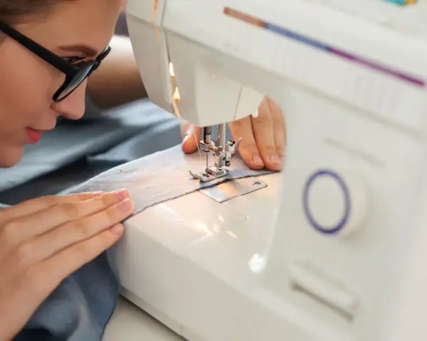 Mujer con gafas concentrada en sus proyectos de costura, cosiendo tela azul en una máquina de coser.