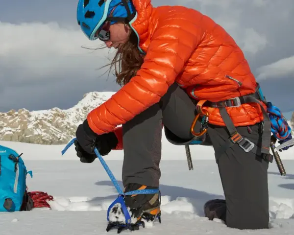 Alpinistka zakłada raki górskie na buty, przygotowując się do wspinaczki w śnieżnych górach.