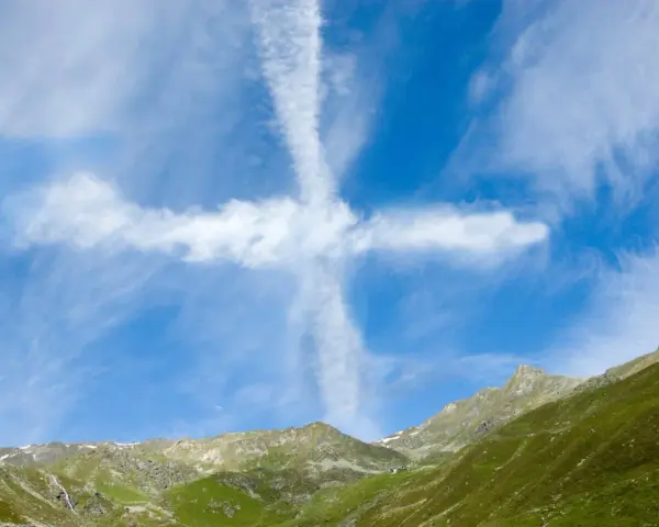 Ein Kreuz aus Wolken am blauen Himmel über grünen Bergen. Man könnte sagen, ihr werdet Zeichen am Himmel sehen.