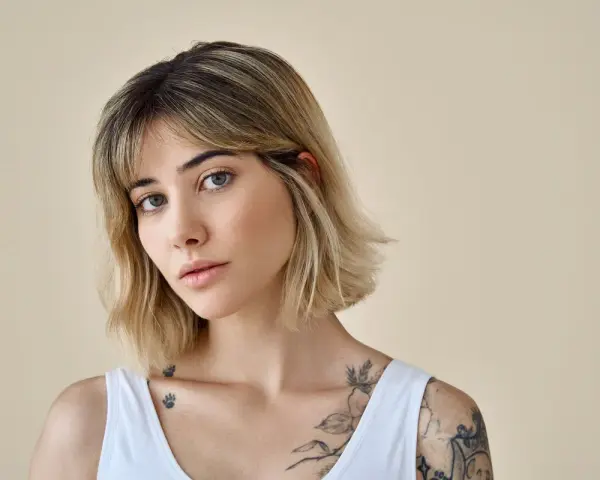 Kobieta z tatuażami na ramionach i dekolcie, z modną fryzurą long bob i grzywką.