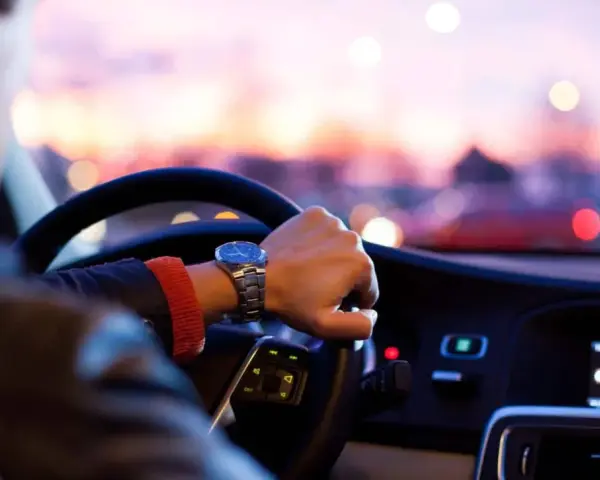 Uomo al volante, con un orologio al polso, pronto per un nuovo uber lavoro al tramonto.