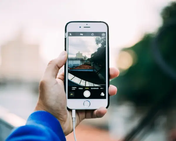 Dłoń trzyma iPhone'a, pokazując ekran z widokiem miasta. Dowiedz się, jak robic zdjecia iphonem, by uchwycić takie ujęcia.