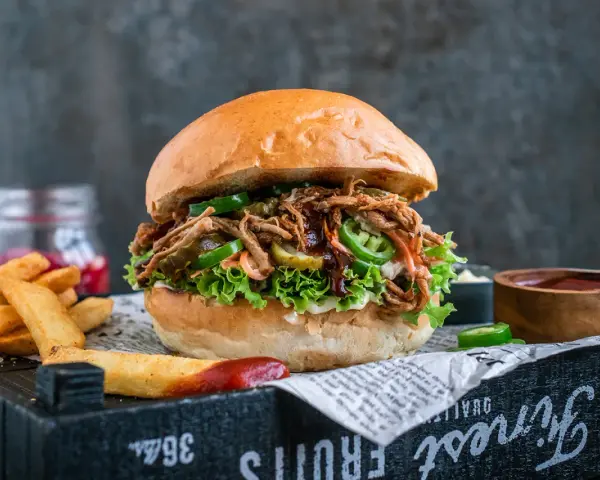 Saftiger pulled pork burger mit Salat, Jalapeños und Gurken. Die Zutaten für diesen Burger sind perfekt aufeinander abgestimmt. Dazu Pommes und Dip.