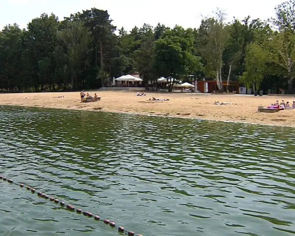 Plaża nad jeziorem Szperek, z kilkoma osobami odpoczywającymi na piasku i wodą w tle.