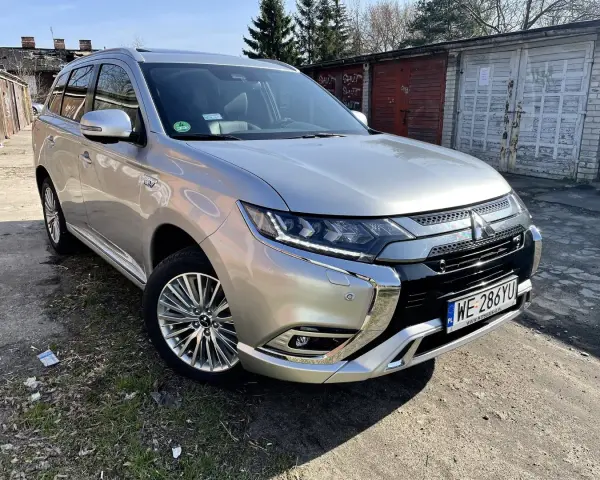 Srebrny Mitsubishi Outlander PHEV na tle garaży. Wiele osób szuka mitsubishi outlander opinie przed zakupem.