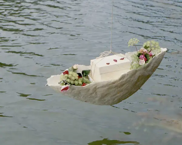Ein Schiffchen mit Blumen und einer Schachtel schwimmt auf dem Wasser. Eine würdevolle Idee für Kinderbeerdigungen.